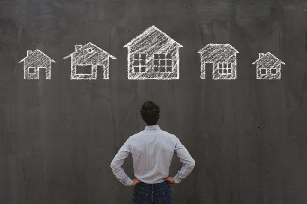 Mann steht vor Tafel auf der Häuser gemalt sind, Symbol für das Thema Berufsbeschreibung Immobilienmakler