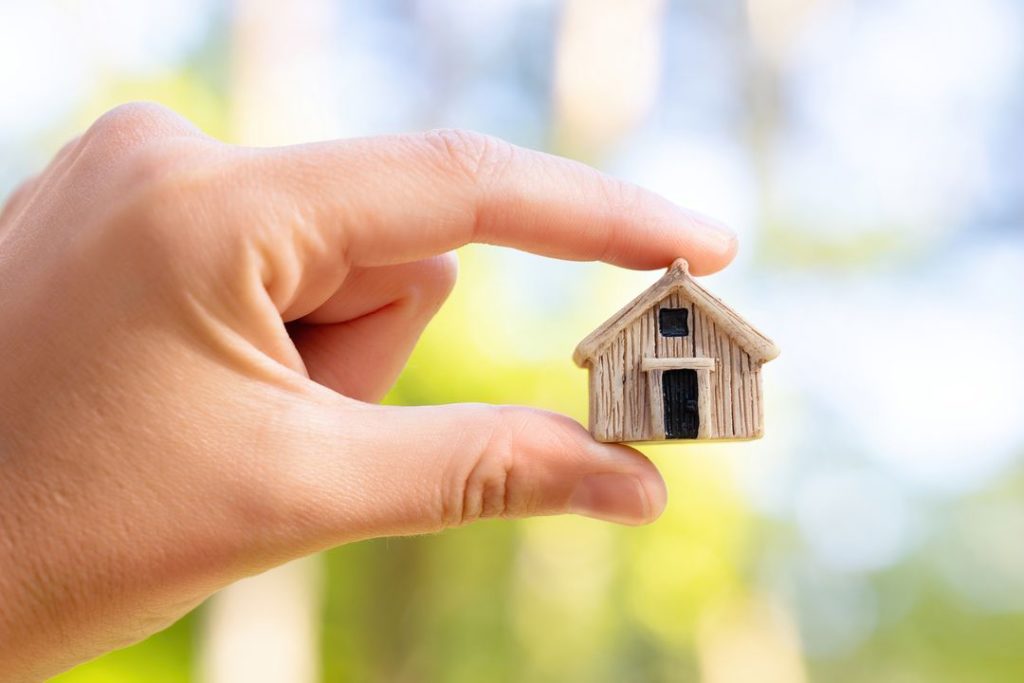 Miniatur Tiny Houses zwischen Zeigefinger und Daumen, Symbol für den Trend Tiny House
