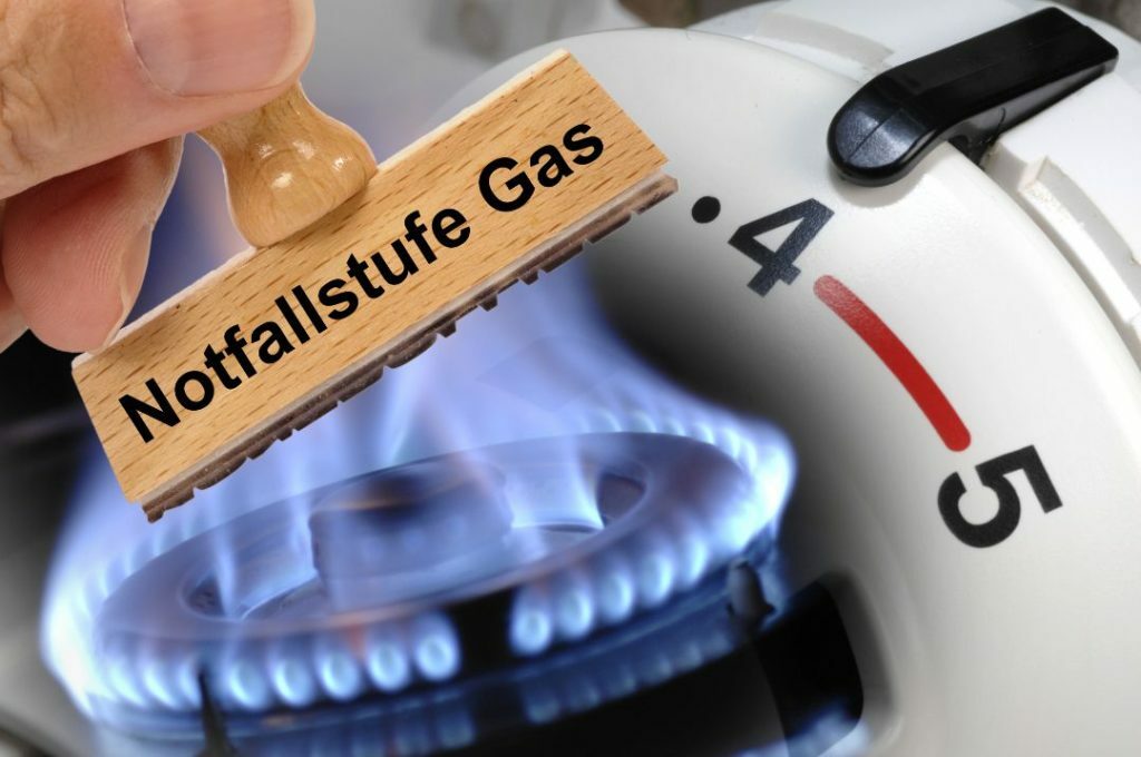 Stempel mit Gas-Notfallstufe über Gasflamme und Heizungsthermostat, verbildlicht, dass Hausbesitzer Gaskosten sparen müssen