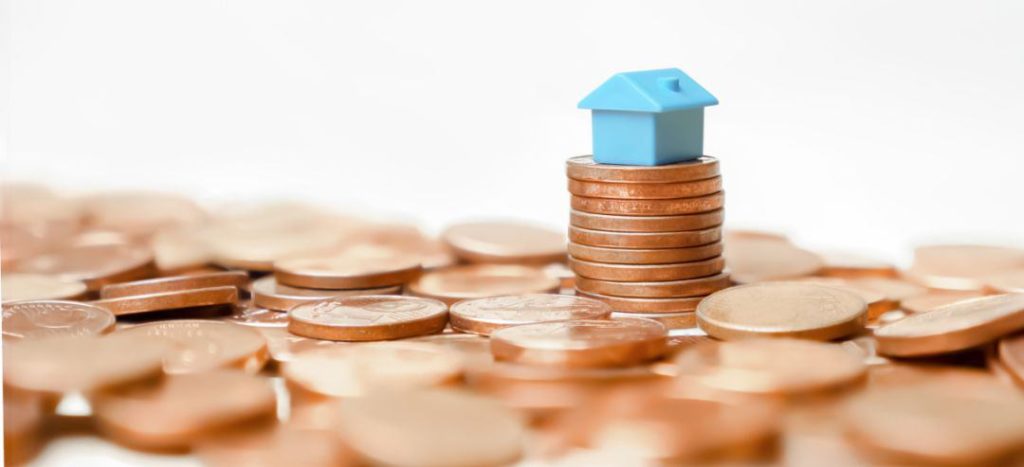 Blaues Modellhaus auf gestapeltem Kleingeld, soll die Schufa-Auskunft bei einer Immobilienfinanzierung verbildlichen
