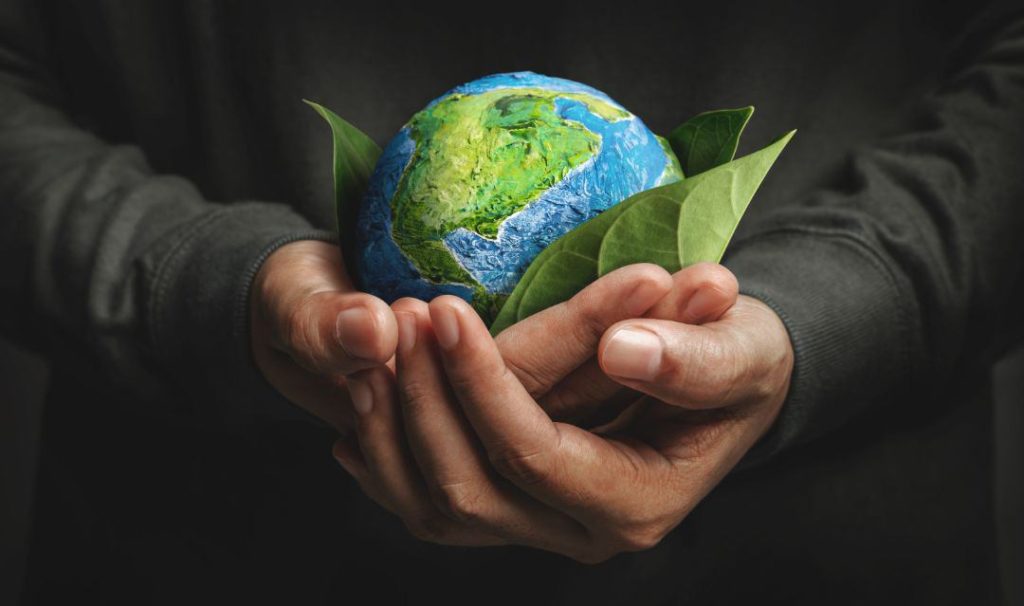 Hand umarmt grünes Blatt und handgefertigten Globus und symbolisiert damit Ökostrom
