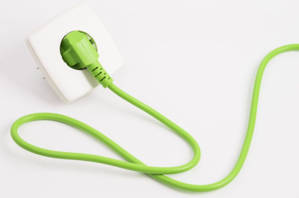 Tipps Stromanbieter wechseln - Grüner Netzstecker in der Steckdose vor weißem Hintergrund
